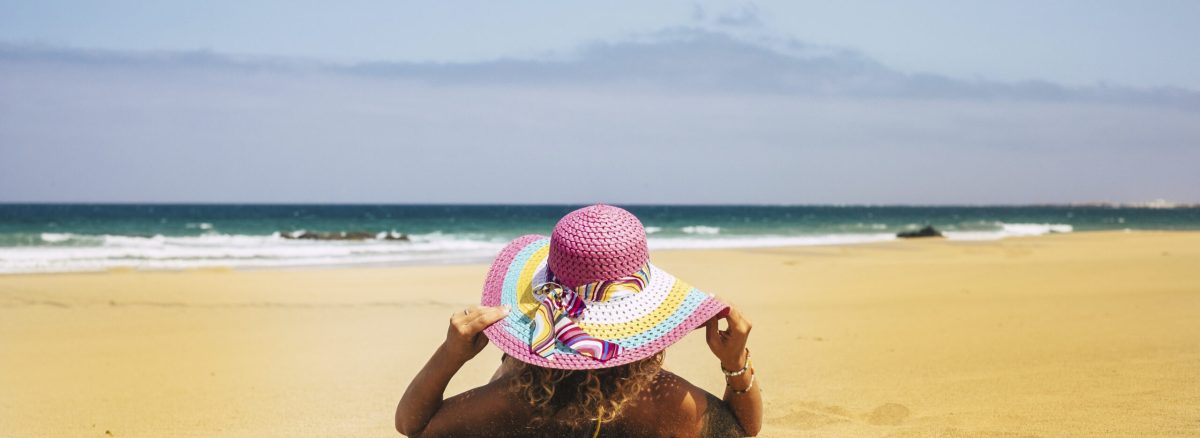 Summer holiday vacation and people relax at the beach concept with woman viewed from back have a sunbath on the sand with sea and blue sky in background - travel and lifestyle
