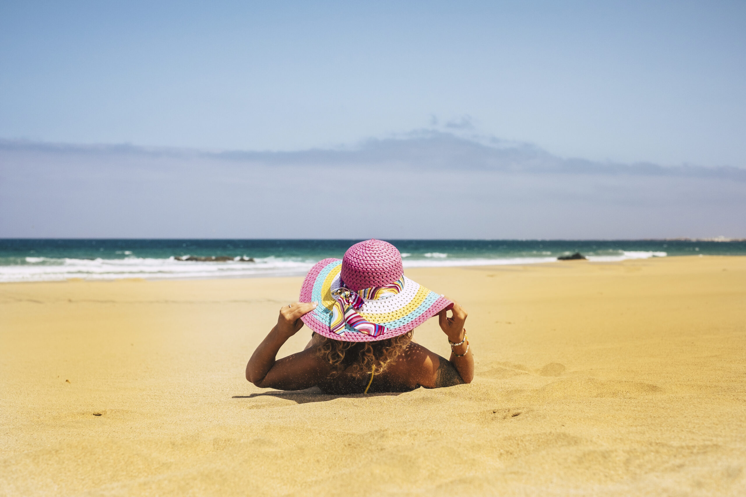 Summer holiday vacation and people relax at the beach concept with woman viewed from back have a sunbath on the sand with sea and blue sky in background - travel and lifestyle
